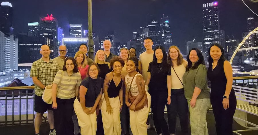 A group of people standing in front of a window with the Singapore skyline behind them.